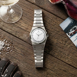 Montre automatique Belvans Daylee cadran blanc posée sur une table en bois dans une scène de voyage.