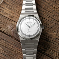 Montre Belvans Daylee cadran blanc et bracelet acier posée sur bois.