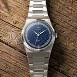 Montre Belvans Daylee cadran bleu et bracelet acier posée sur bois.