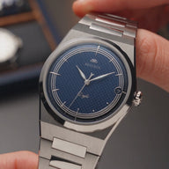 Gros plan vertical de la montre automatique Belvans Daylee au cadran bleu tenue en main
